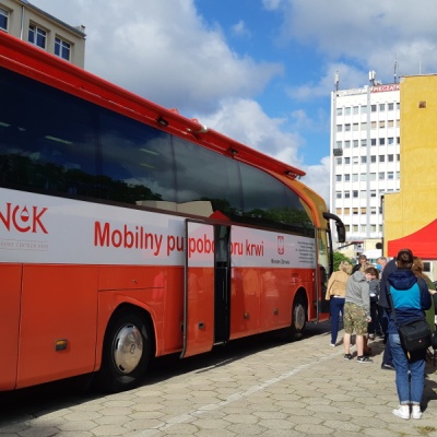 Czerwony autobus z Regionalnego Centrum Krwiodawstwa i Krwiolecznictwa w Szczecinie, po prawej stronie kolejka osób chętnych do oddania krwi.