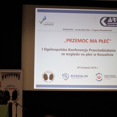 Pan Przemysław Krzyżanowski na tle ekranu zawierającego nazwę konferencji, termin, organizatorów i źródło finansowania