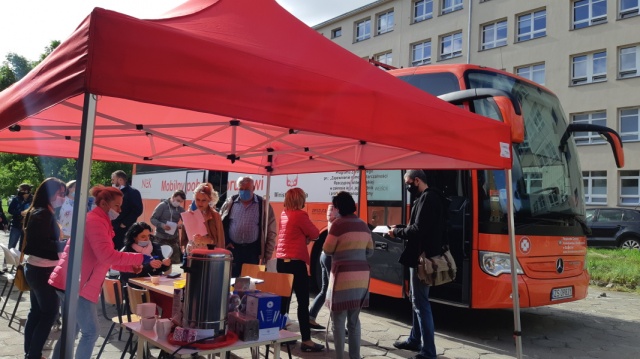 Na tle Mobilnego Punktu Poboru Krwi pracownicy MOPR wydają ankiety osobom chętnym do udziału w akcji krwiodawstwa.